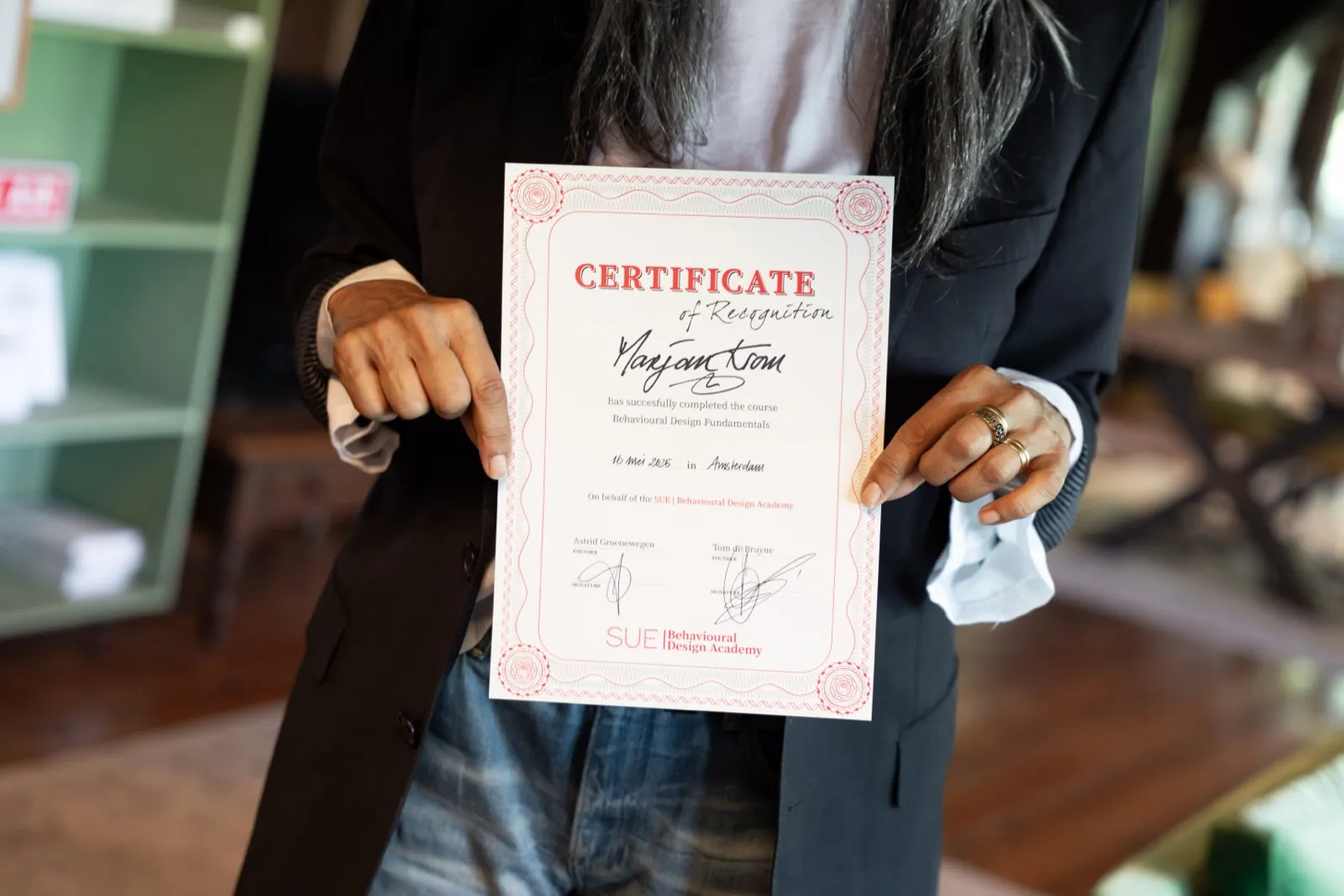 Participant shows the certificate of the Behavioural Design Fundamentals course, signed by Astrid Groenewegen and Tom de Bruyne